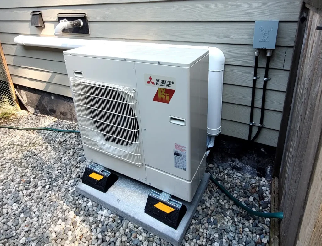 Mitsubishi Electric heat pump outdoor unit installed on concrete pad beside gray house