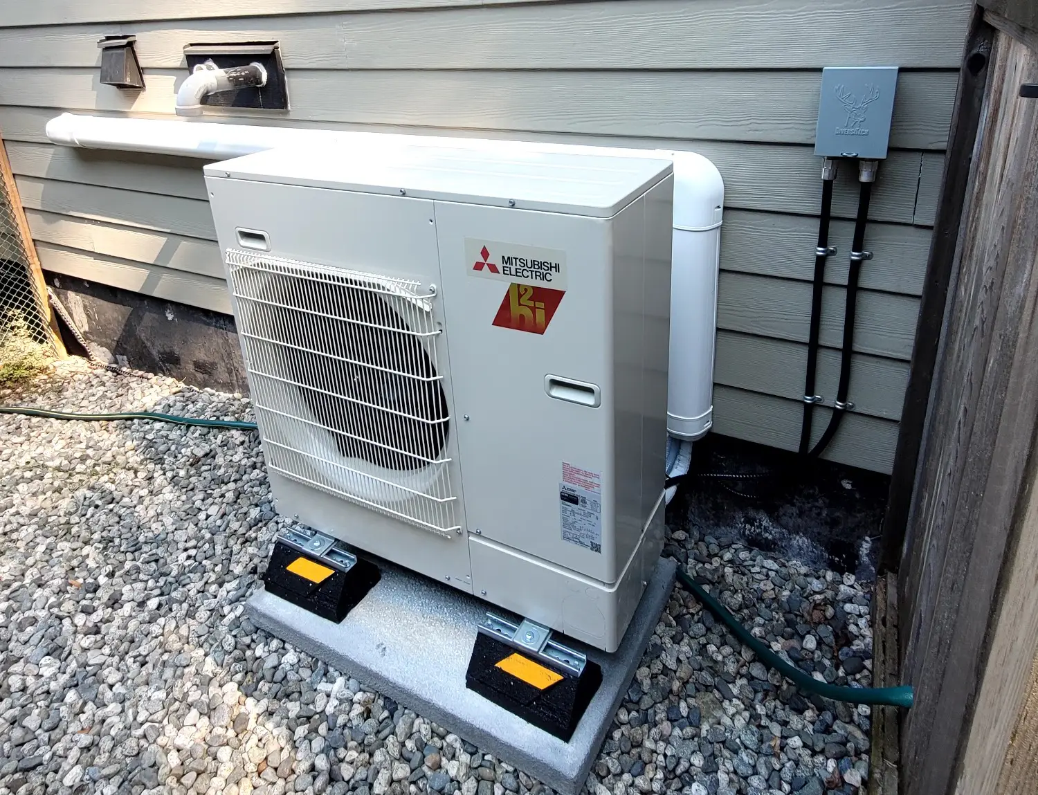 Mitsubishi Electric heat pump outdoor unit installed on concrete pad beside gray house