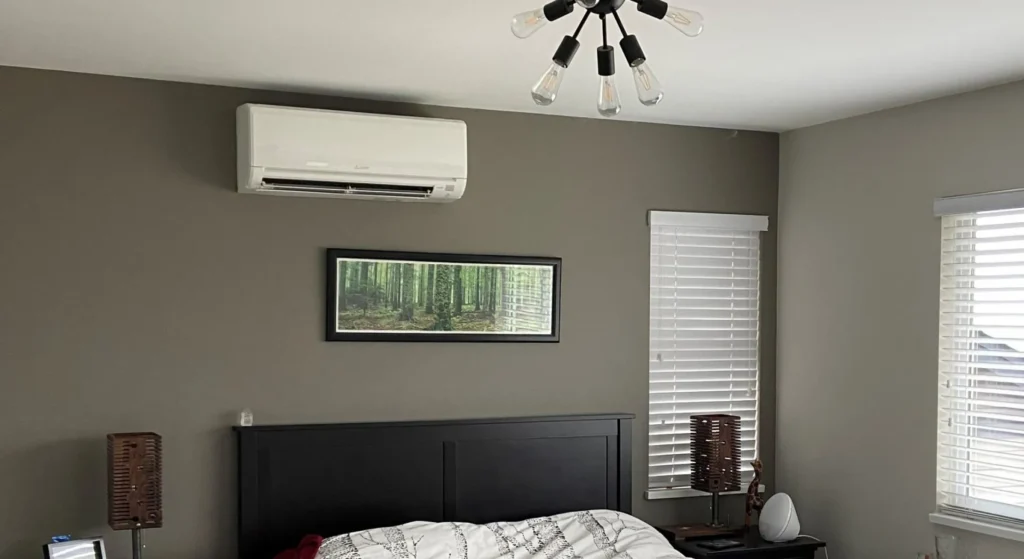 White mini-split air conditioning unit mounted on gray bedroom wall above black headboard
