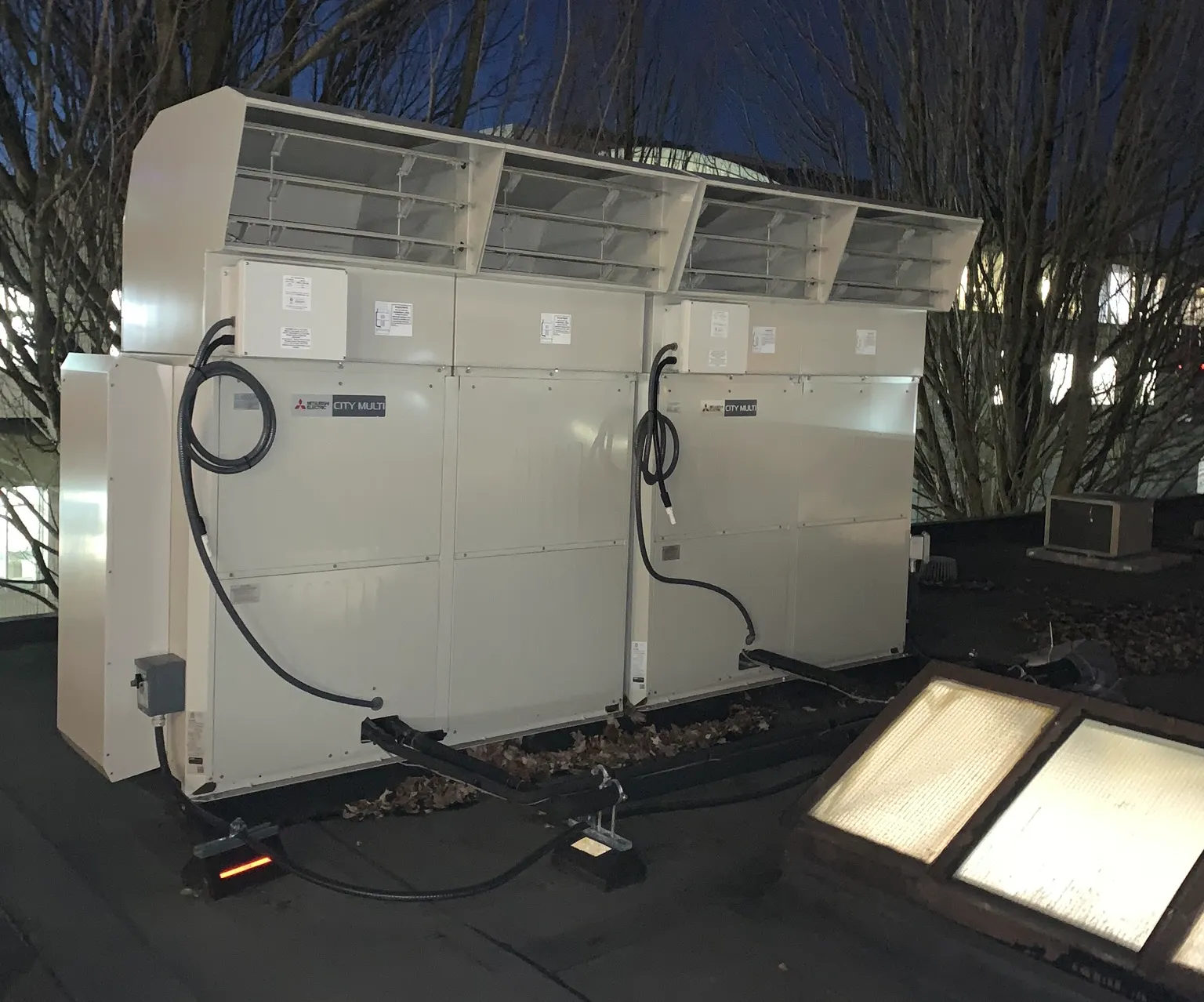 Multiple white Mitsubishi HVAC units with connecting cables during evening installation