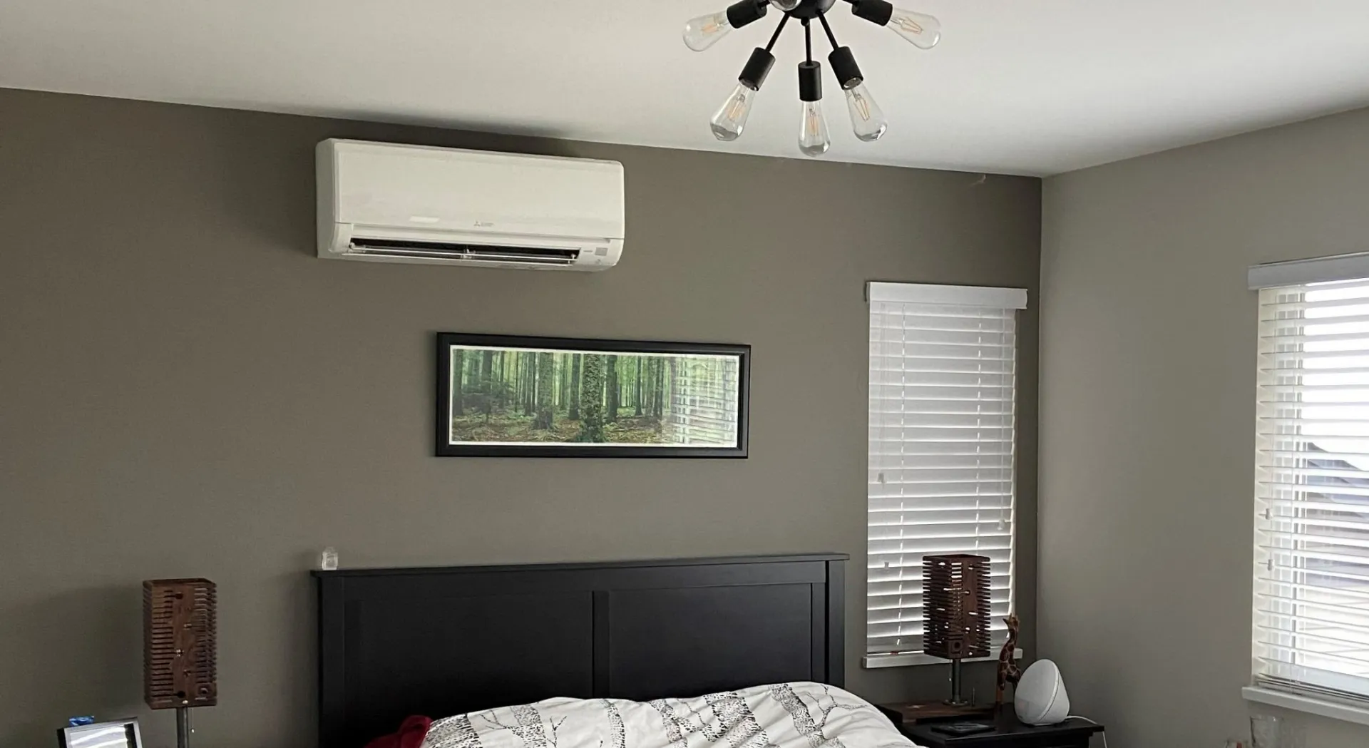 White mini-split air conditioning unit mounted on bedroom wall above dark wooden headboard