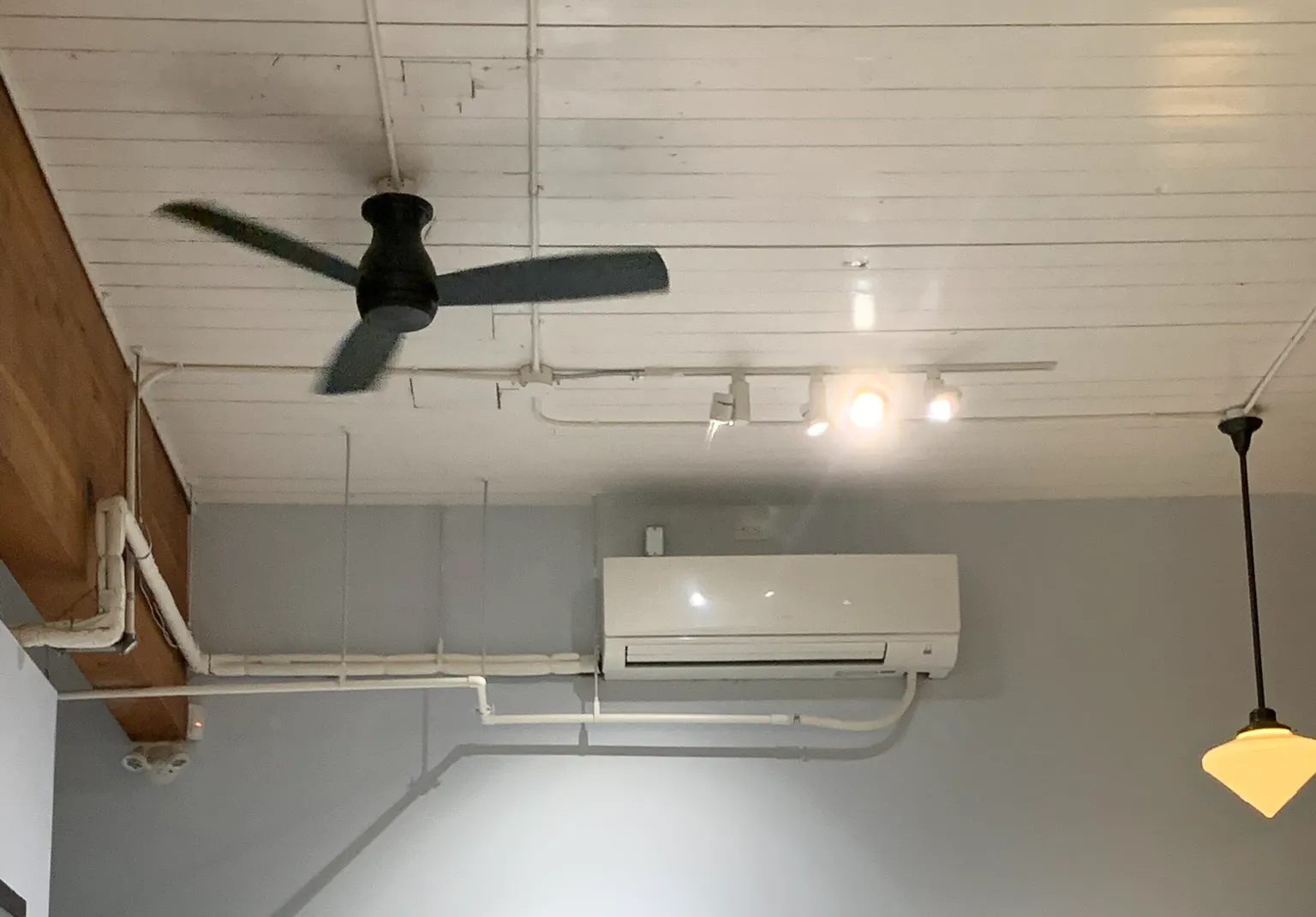 Ceiling-mounted mini-split unit with exposed white ceiling beams and black ceiling fan