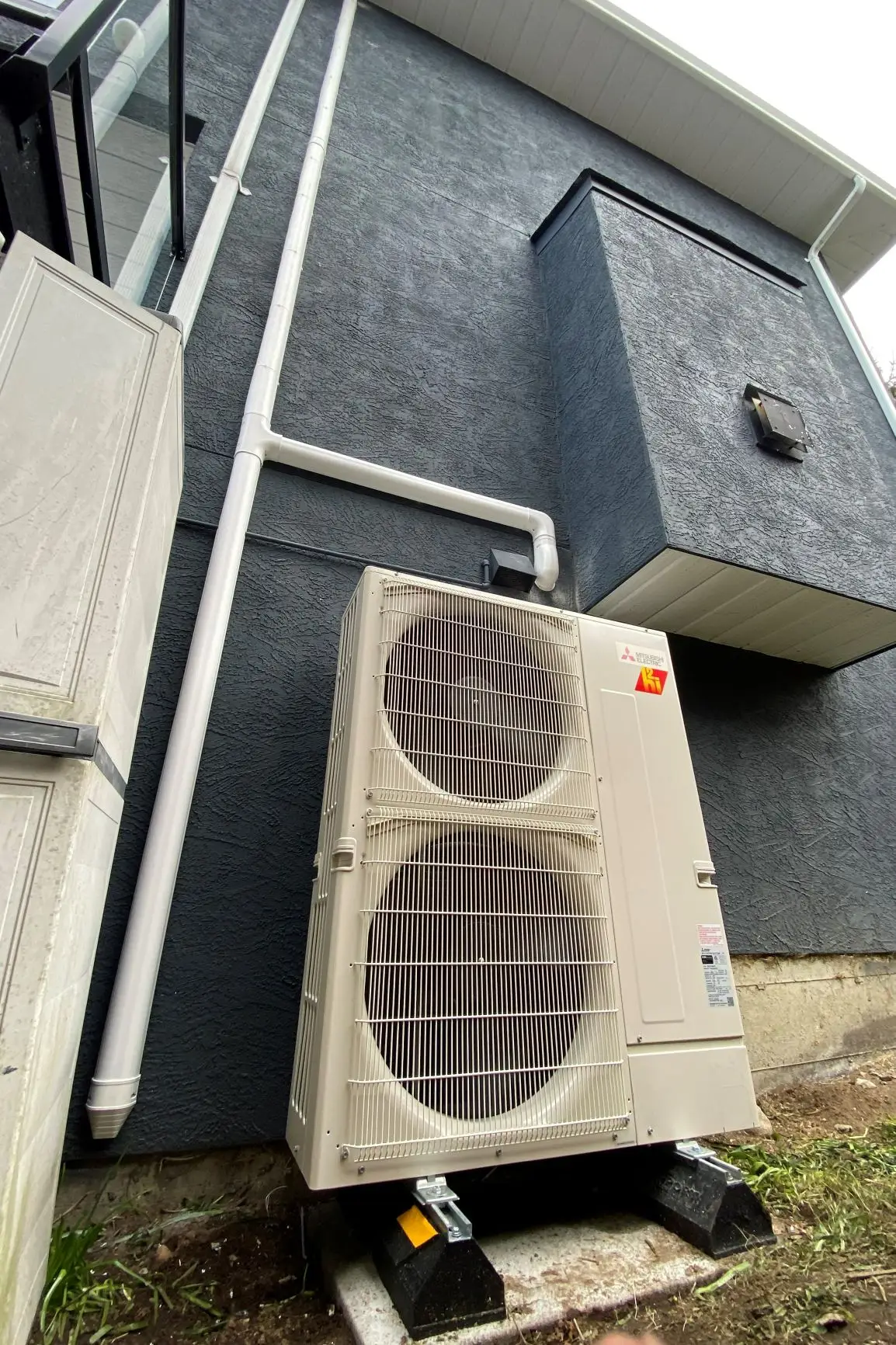 Mitsubishi Electric outdoor condenser on concrete pad with white PVC line-set cover against dark stucco exterior wall