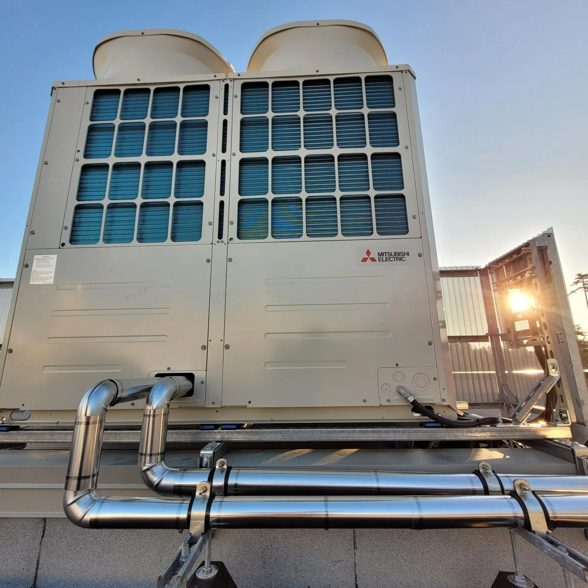 Large Mitsubishi Electric VRF rooftop unit with polished refrigerant lines on shingled roof at sunset