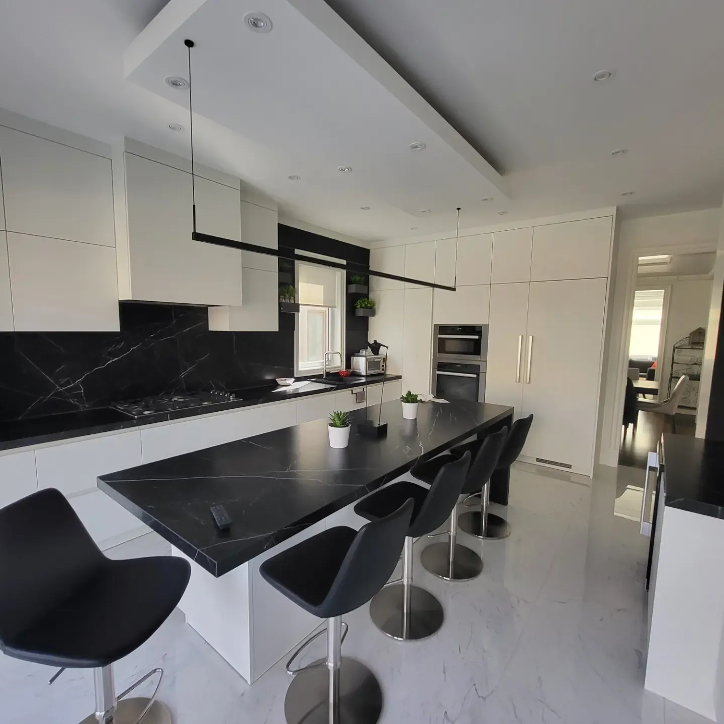 Modern black and white kitchen with marble island, bar stools, and white flat-panel cabinets in Toronto home