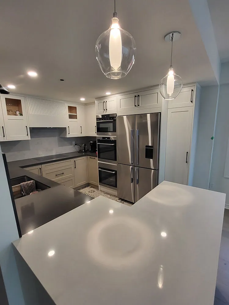 Kitchen renovation showing white shaker cabinets, stainless steel appliances, dark countertops, and glass pendant lights